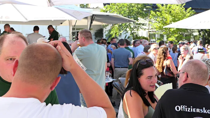 Menschen unterhalten sich bei einem Schützenfest-Warm-up im Freien unter weißen Sonnenschirmen.