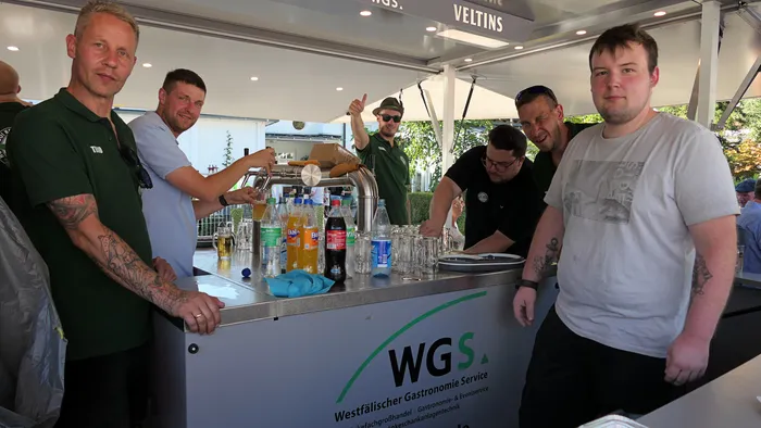 Männer an einem Tresen mit Getränken und Gläsern bereiten ein Schützenfest-Warm-up vor.