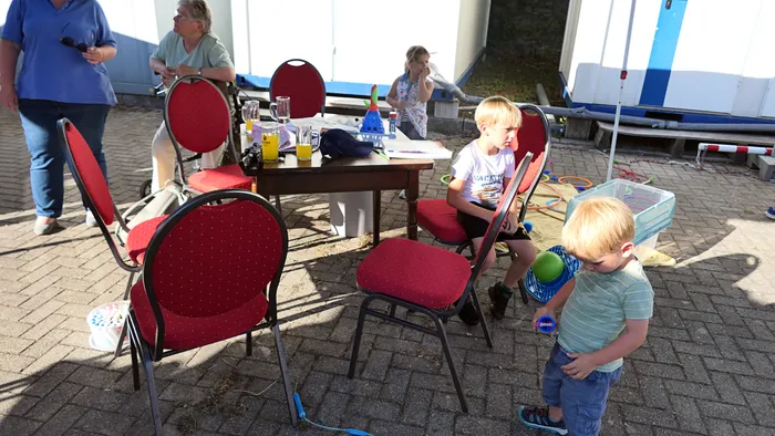 Kinder und Erwachsene versammeln sich im Freien an einem Tisch mit Getränken während eines Schützenfest-Warm-ups.