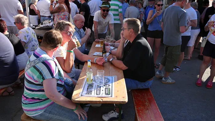 Menschen sitzen an langen Holztischen im Freien und trinken gemeinsam Bier.