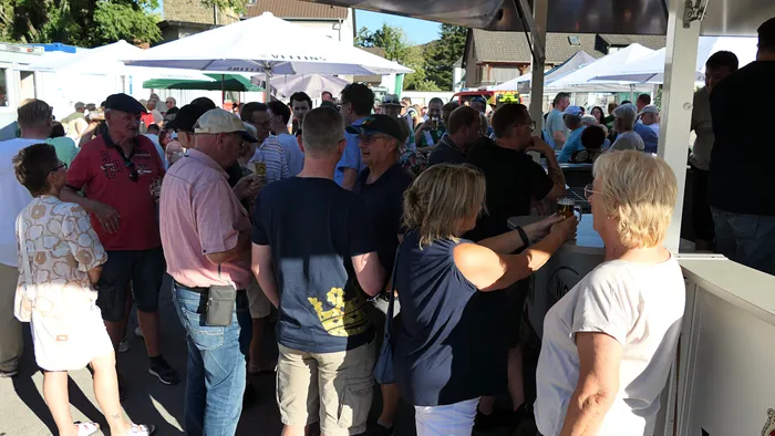 Menschen versammeln sich bei einem Schützenfest-Warm-up unter weißen Zelten und Sonnenschirmen.