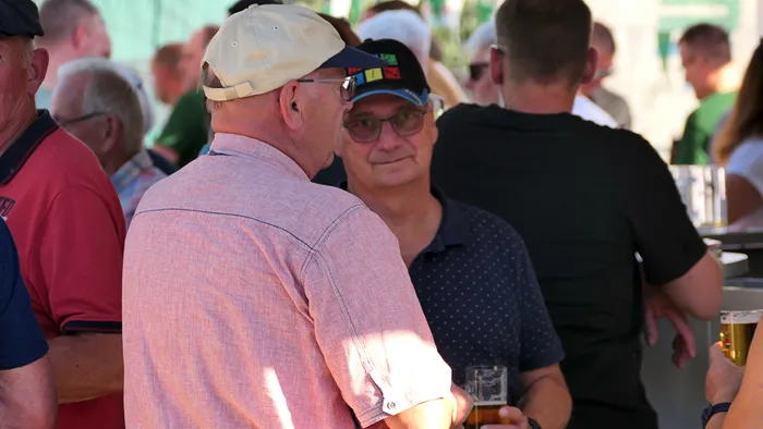 Männer stehen bei einem geselligen Beisammensein im Freien zusammen, einige halten Biergläser.