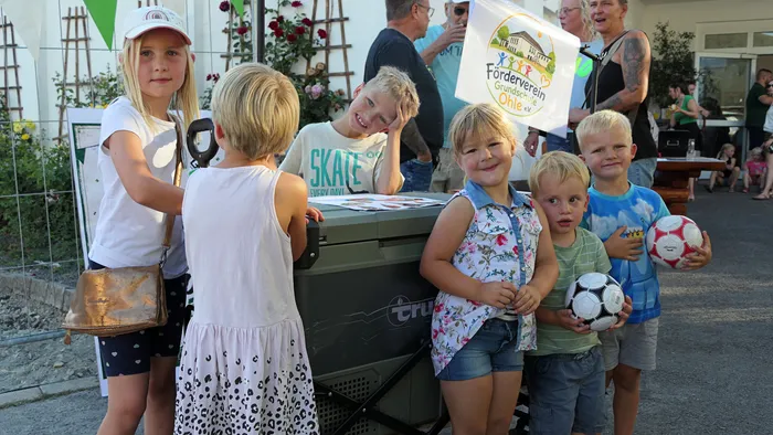 Kinder posieren mit Fußbällen neben einer Kühlbox; im Hintergrund weht eine Flagge des Fördervereins Grundschule Ohle.