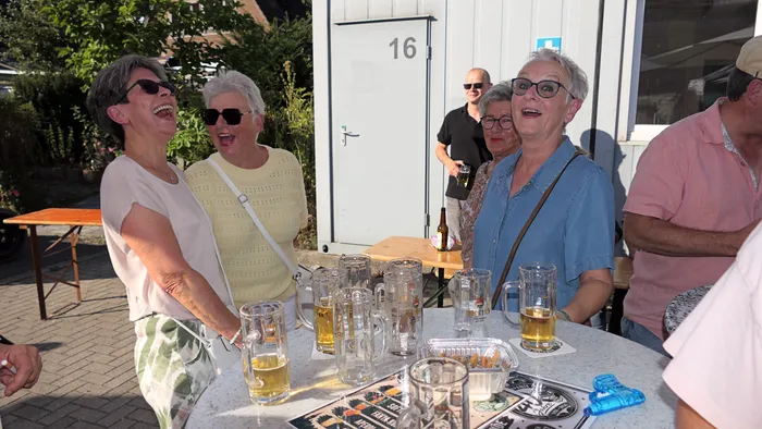 Lachende Menschen stehen an einem Tisch mit Bierkrügen im Freien während eines Schützenfest-Warm-ups.