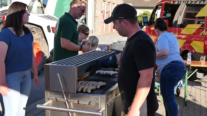 Menschen grillen Würstchen auf einem großen Metallgrill im Freien.