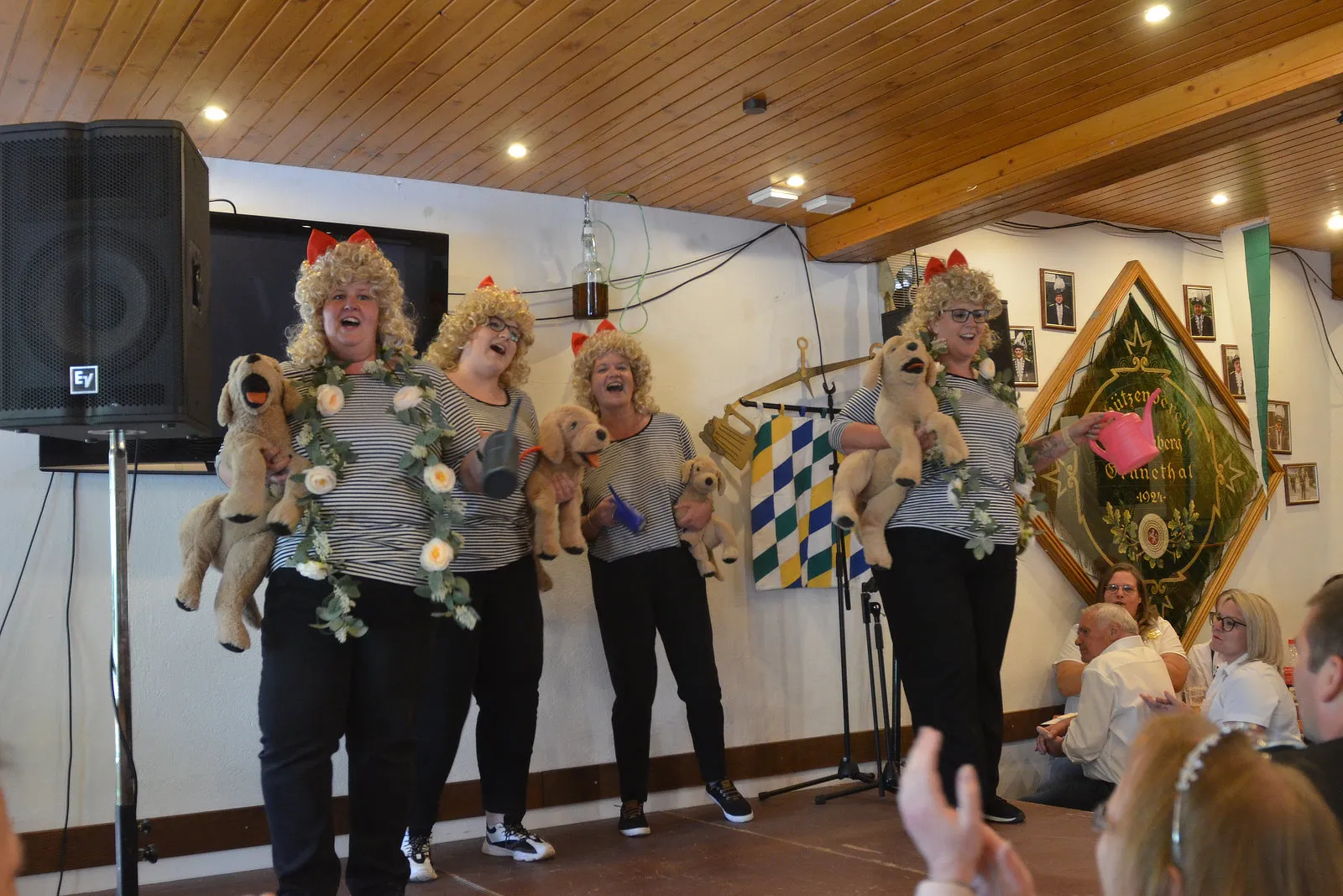 Fünf Personen mit blonden Perücken und gestreiften Oberteilen führen auf einer Bühne eine Puppenspiel-Performance auf.