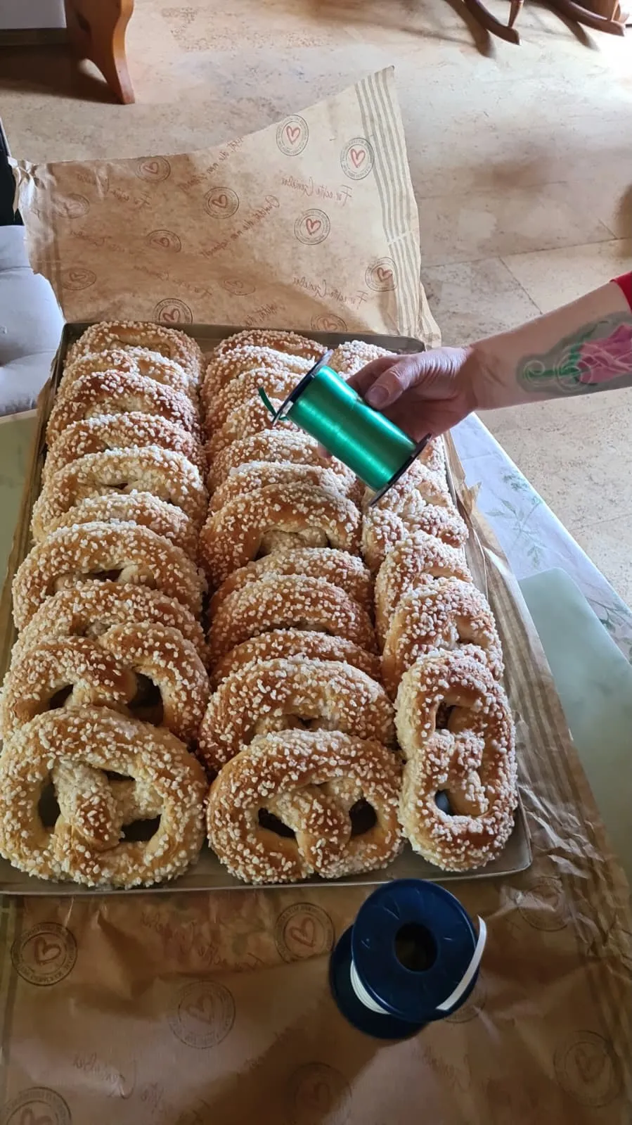 Mehrere Reihen Sesamringe liegen in einer Schachtel. Eine Hand bindet ein grünes Band um die Süßspeise.