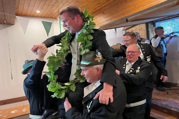Ein Mann wird von einem anderen mit einem grünen Kranz um den Hals geschmückt, während mehrere Männer in Uniformen im Hintergrund stehen. Der Schützenverein Grünetal eröffnete die Saison mit dem Abschuss des Vogels durch Christian Hoffmann.