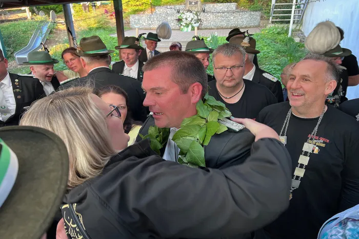 Christian Hoffmann wird nach dem Abschuss des Vogels von einer Frau umarmt, umgeben von Schützen in traditioneller Kleidung.