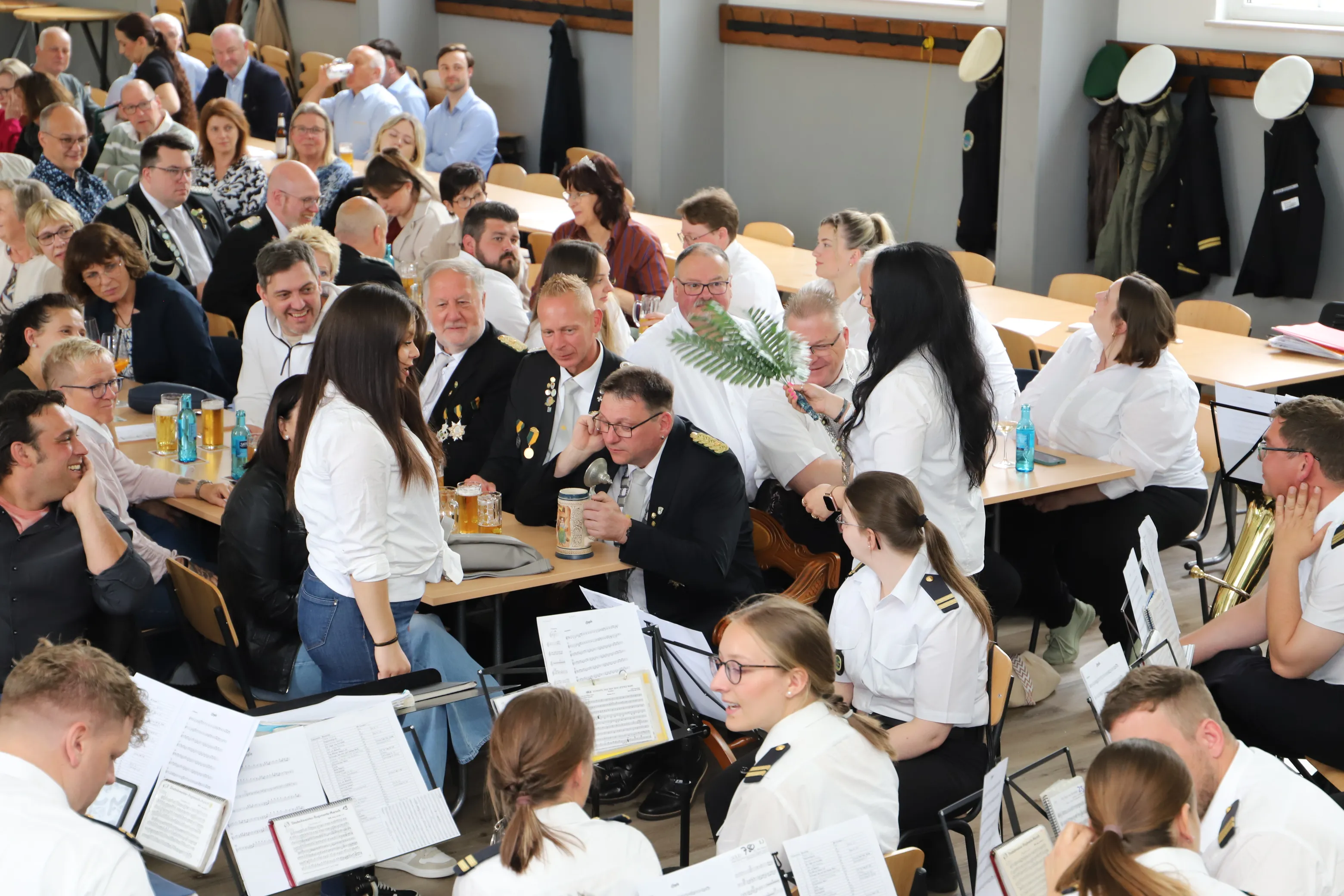 Große Menschenmenge bei einem Schützenfest, viele Personen in Uniformen sitzen an Tischen und lachen, während einige auf einer kleinen Bühne stehen.