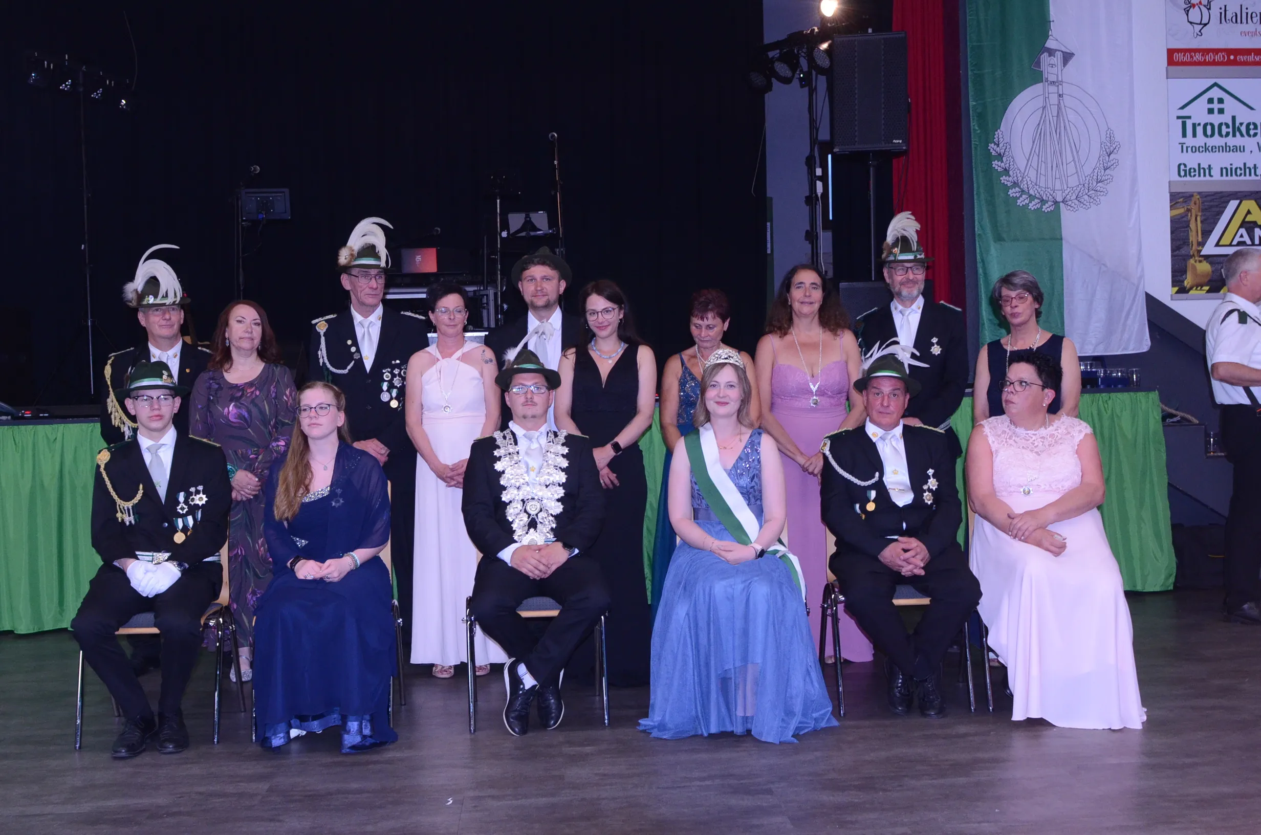Gruppenfoto von zehn Personen in festlicher Kleidung auf einer Bühne, darunter Mitglieder einer Schützenkompanie und das frisch gekrönte Königspaar mit Krone und Ordensband.