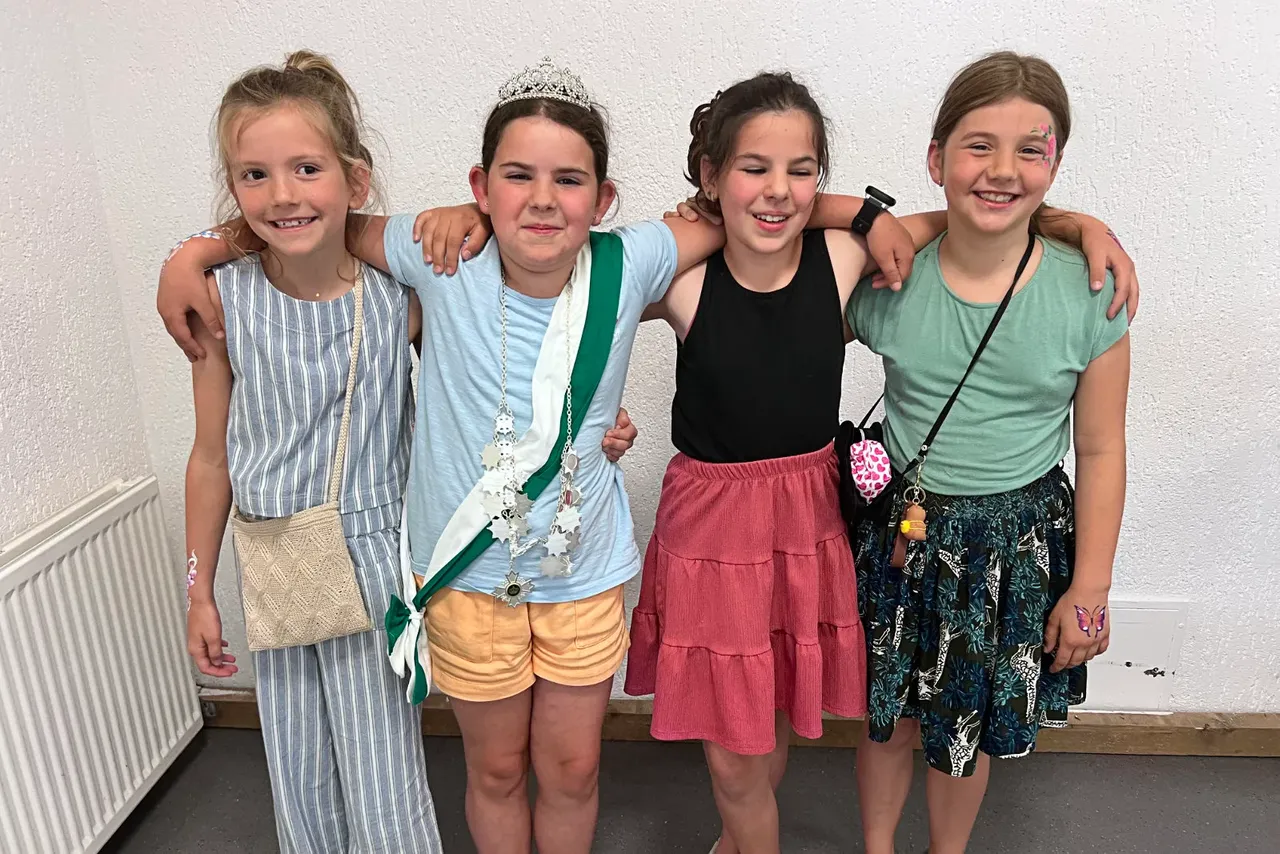 Vier Mädchen umarmen sich, die Mitte trägt eine Krone und ein Schützenabzeichen. Die neue Kinderschützenkönigin Elisa Bongiovanni steht mit ihren Freundinnen vor einer weißen Wand.