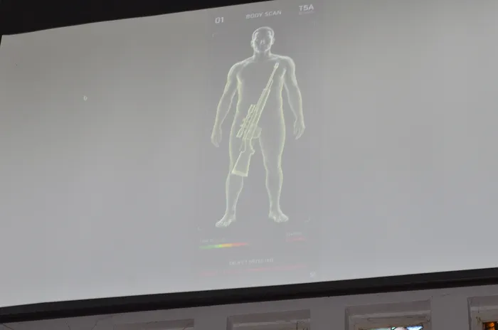 Ein Körper-Scan zeigt die Silhouette einer Person mit einem Gewehr. Der Scan-Status zeigt 
