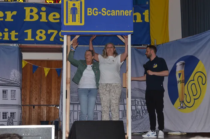 Zwei Frauen und ein Mann stehen auf einer Bühne vor einem Banner mit der Aufschrift 