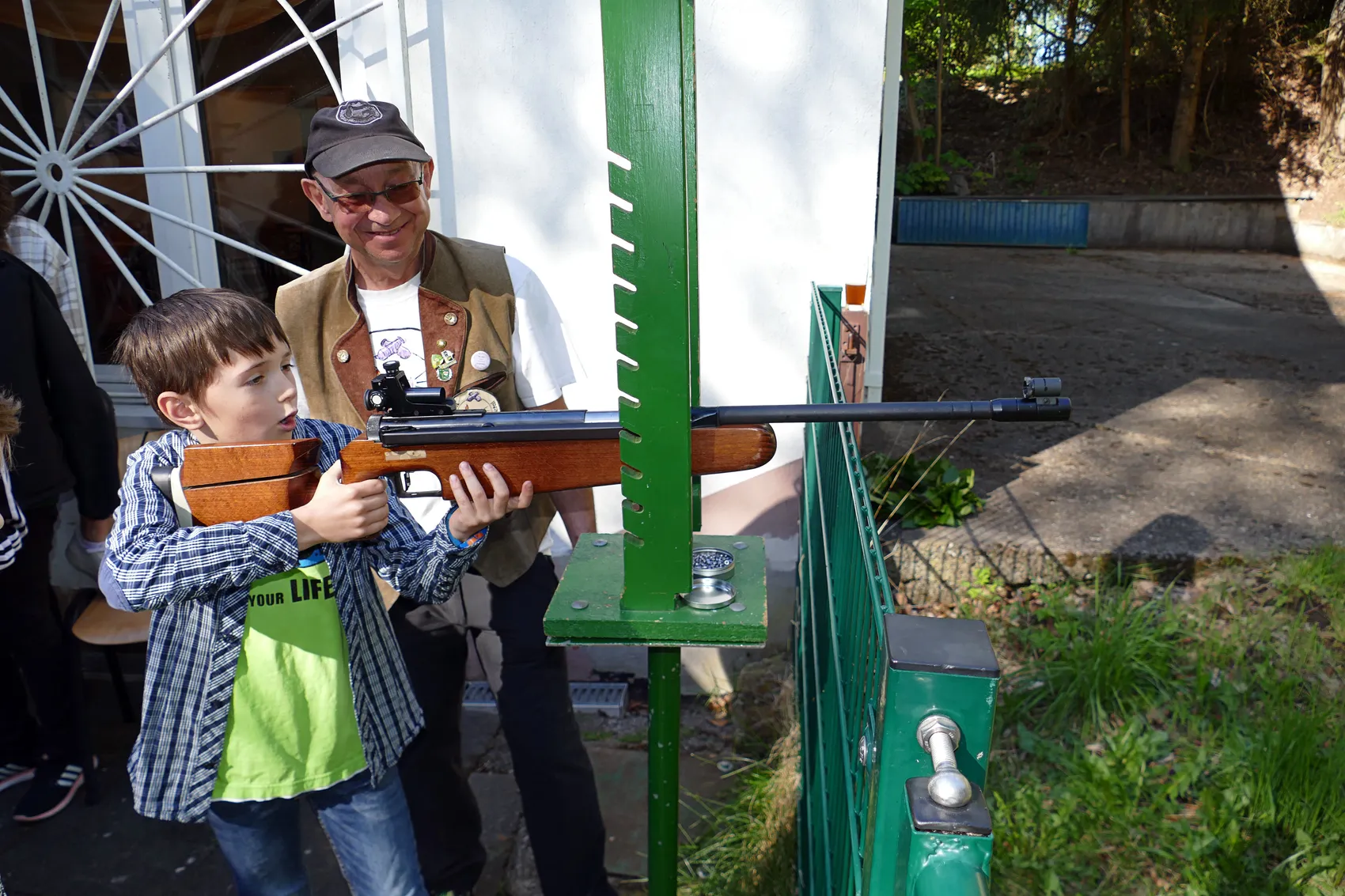 Ein Mann hilft einem Jungen beim Zielen mit einem Luftgewehr auf einer Schießanlage im Freien.