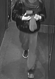 Schwarz-Weiß-Aufnahme einer Person, die eine Jacke und Hose trägt und eine Tasche hält.