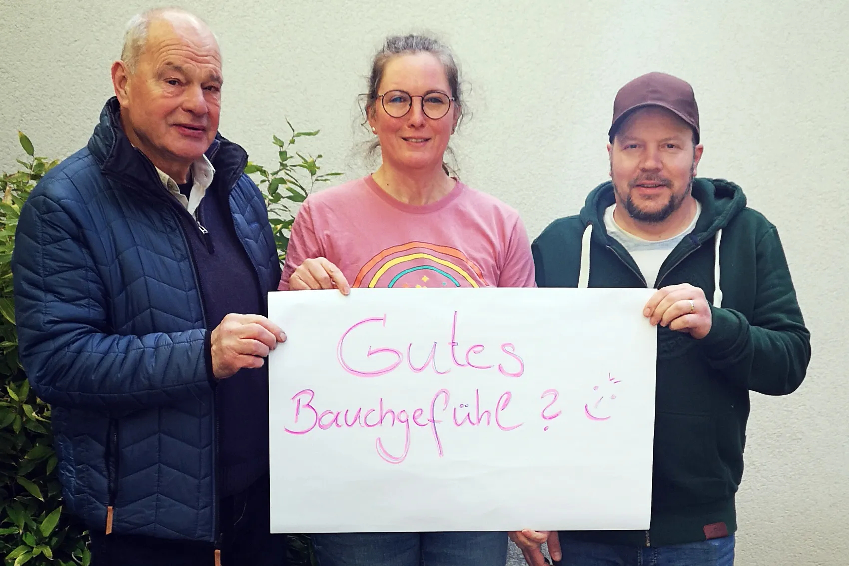 Drei Personen halten ein Schild mit der Aufschrift „Gutes Bauchgefühl?“ in die Kamera. Links Wolfgang Selter, in der Mitte Mareike Masuch und rechts Dominic Six.