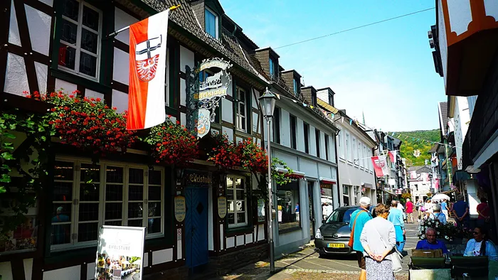 Blick auf eine Straße in der historischen Altstadt von Ahrweiler mit Fachwerkhäusern, Blumenkästen und Passanten.