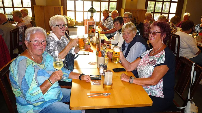 Eine Gruppe älterer Menschen sitzt bei Getränken an einem langen Holztisch in einem Restaurant während eines Ausflugs.