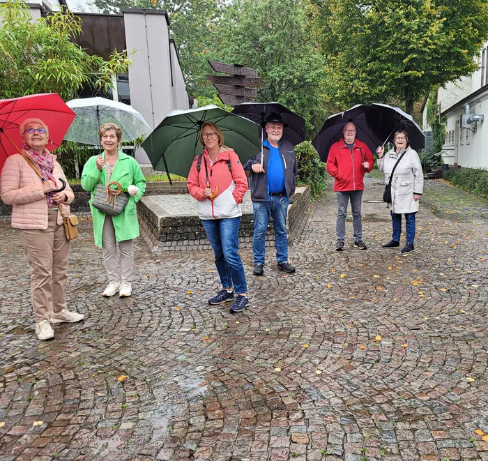 Sechs Personen mit Regenschirmen stehen auf einem nassen Kopfsteinpflasterweg während einer Innenstadtbegehung.