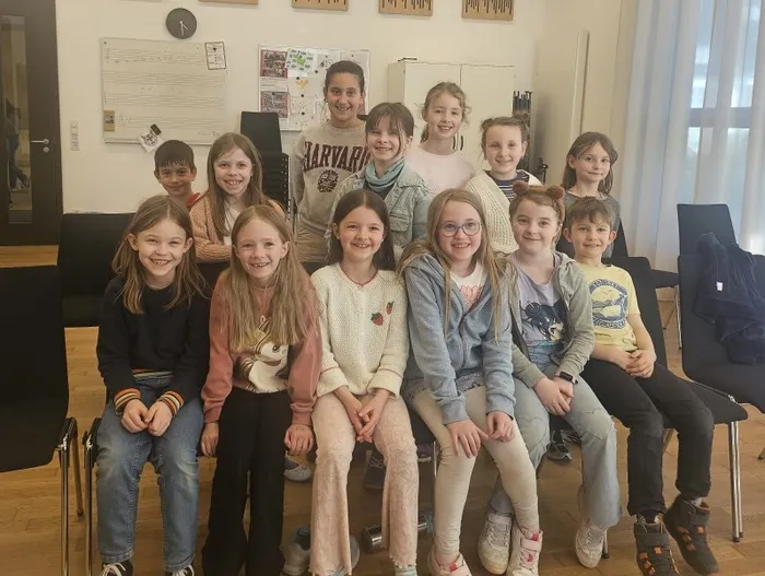 Eine Gruppe von Kindern und Jugendlichen lächelt in die Kamera. Sie stehen und sitzen vor einer hellen Wand mit Pinnwänden und Bildern.