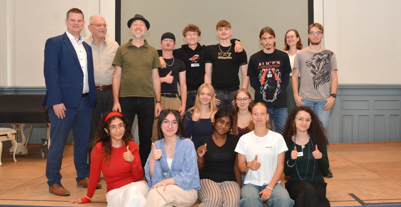Eine Gruppe von Schülern und drei Männern posiert für ein Gruppenfoto und zeigt teilweise den Daumen nach oben.