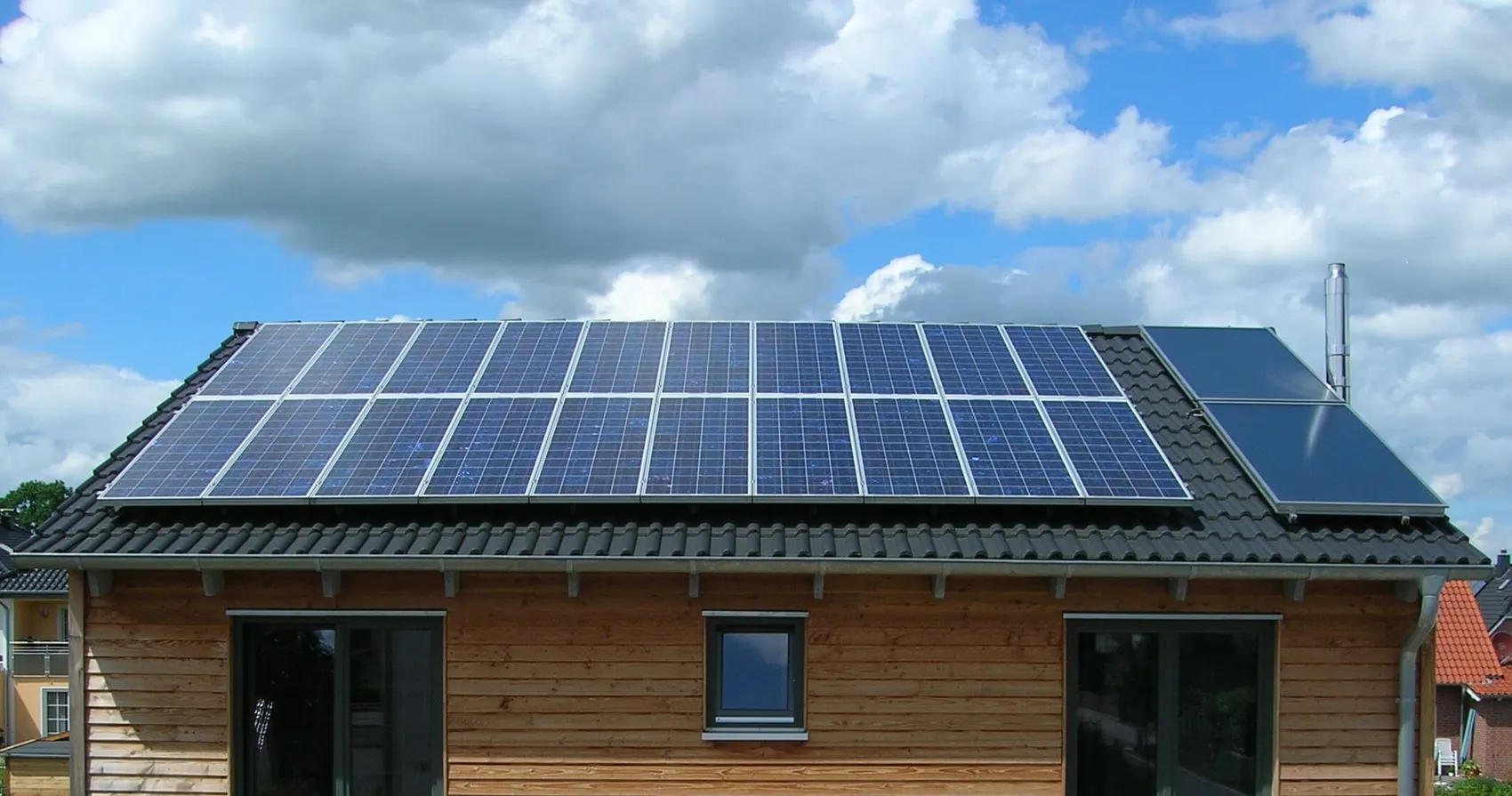 Ein Holzhaus mit Solarmodulen auf dem Dach unter einem bewölkten Himmel.