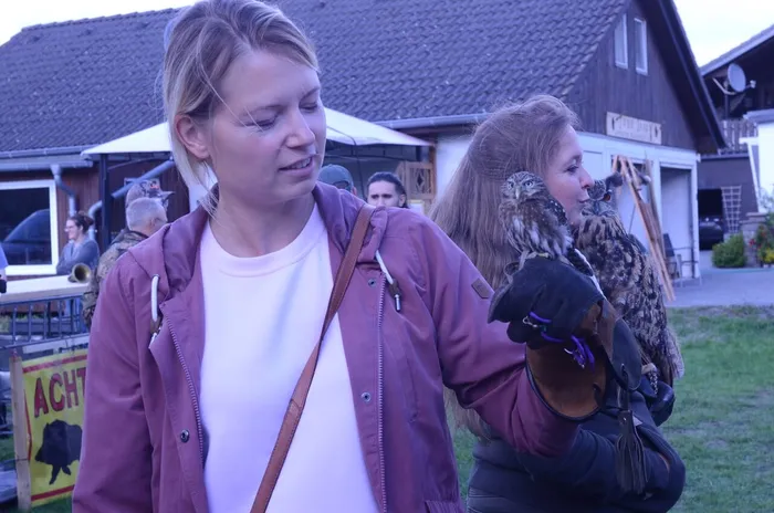 Eine Frau betrachtet eine kleine Eule auf ihrer behandschuhten Hand, während im Hintergrund eine weitere Person eine größere Eule hält.