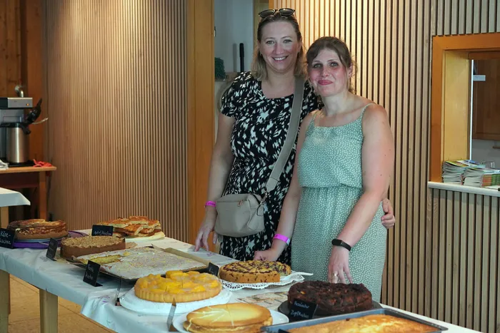Zwei Frauen stehen lächelnd hinter einem Tisch mit verschiedenen Kuchen und Torten. Im Hintergrund ist eine Holzverkleidung und ein Teil eines Buffets zu sehen.