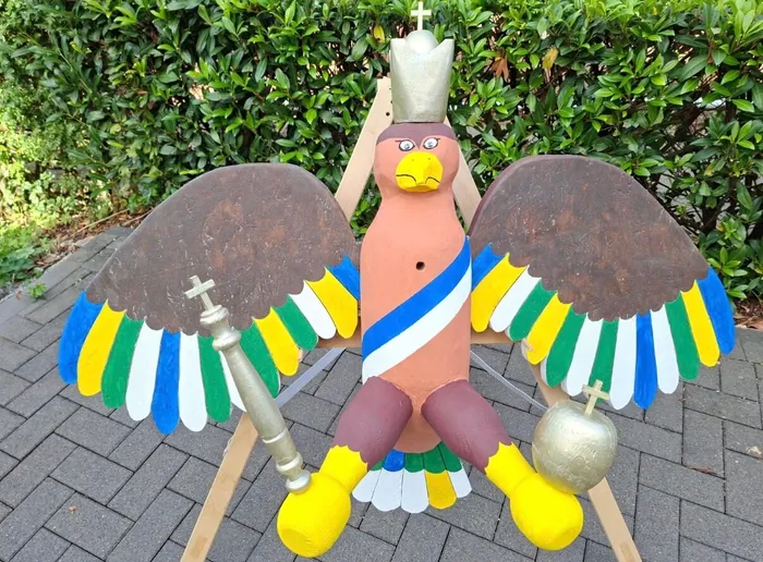 Bunt bemalte Holzfigur eines Vogels mit Krone, Zepter und Reichsapfel auf einem Holzgestell.