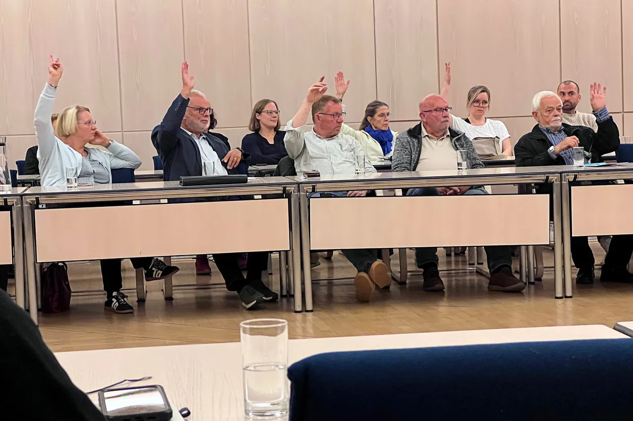 Mehrere Personen sitzen an einem langen Tisch und heben ihre Hände zur Abstimmung.