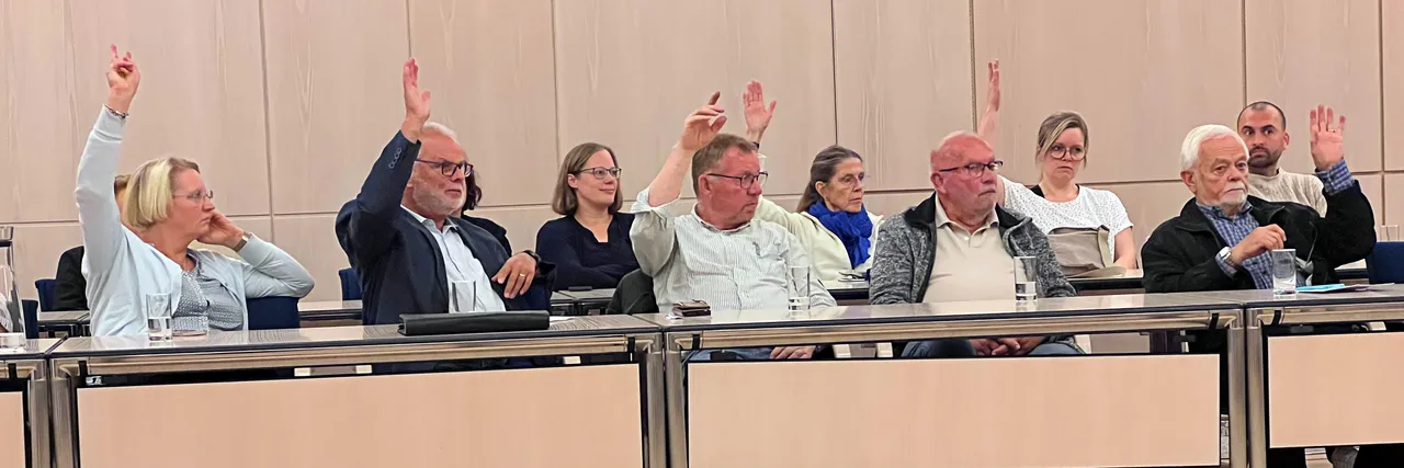 Mitglieder in einem Sitzungssaal halten ihre Hände zur Abstimmung nach oben.