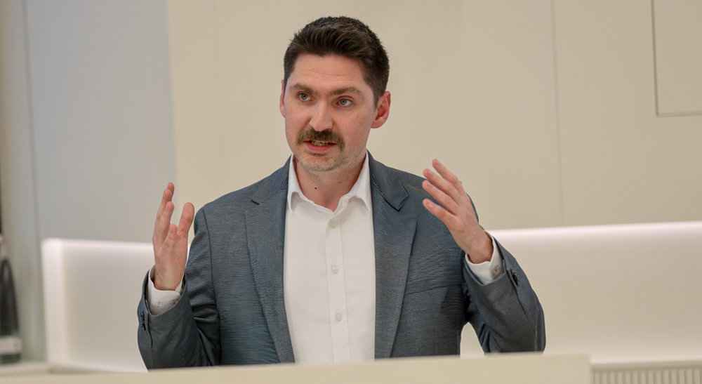 Steffen Wieland, erkennbar an seinem Schnurrbart, gestikuliert während einer Rede oder Präsentation.