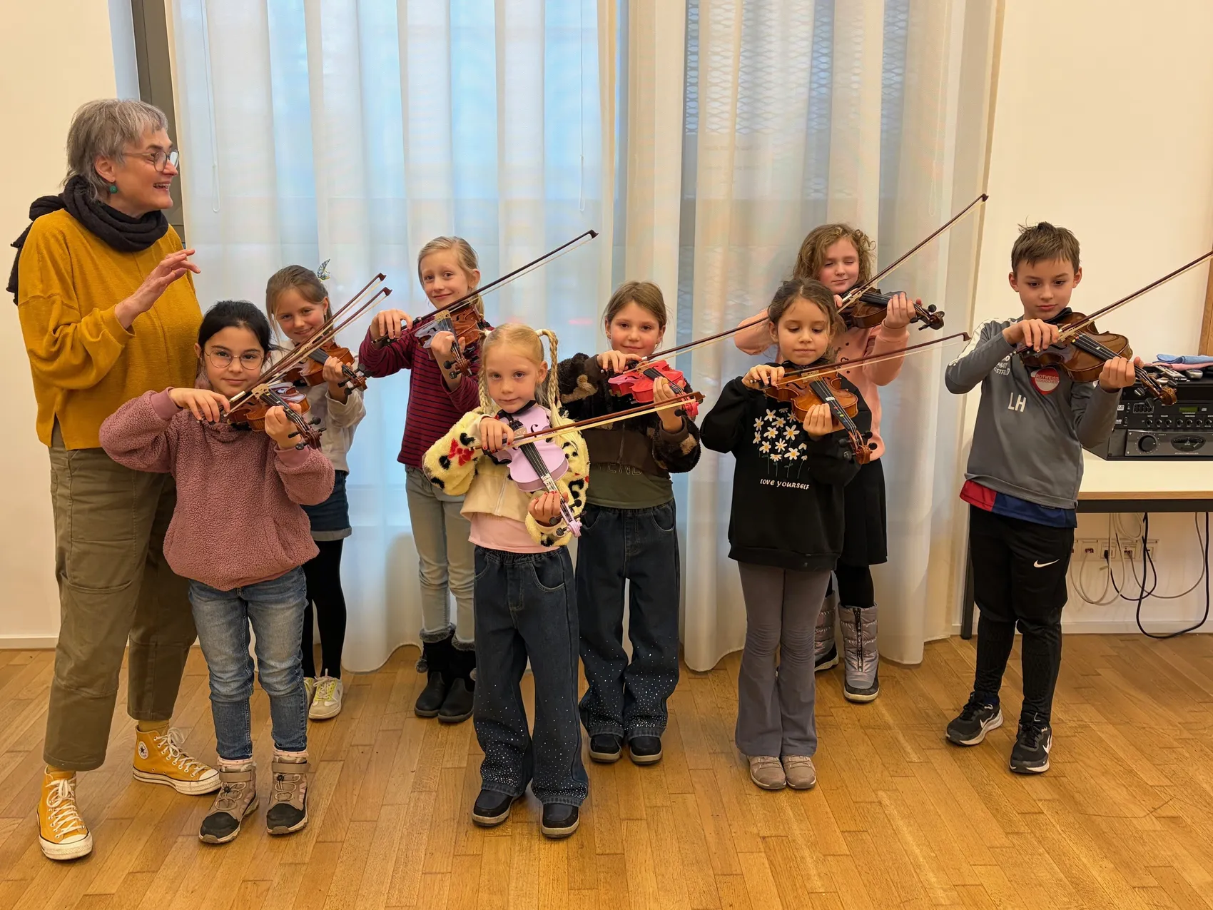 Eine Gruppe von Kindern und Jugendlichen spielt Violine unter Anleitung einer Frau. Sie bereiten sich auf ein Konzert vor.