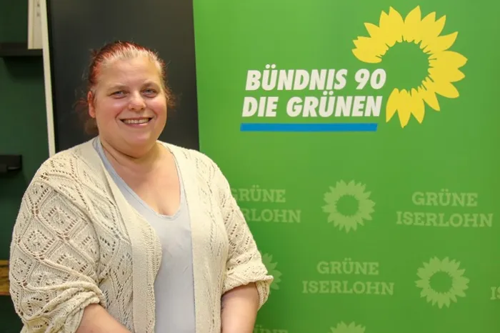 Sylvia Olbrich vor grünem Hintergrund mit dem Logo von Bündnis 90/Die Grünen und dem Hinweis auf die Grünen Iserlohn.