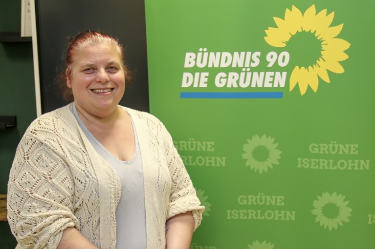 Sylvia Olbrich vor grünem Hintergrund mit dem Logo von Bündnis 90/Die Grünen und dem Hinweis auf die Grünen Iserlohn.