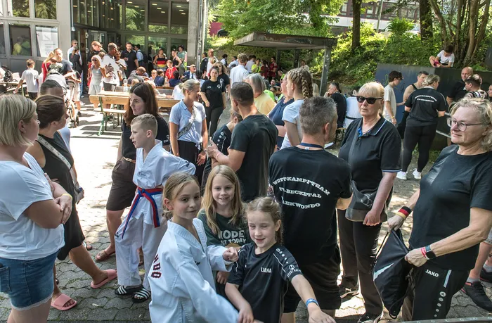 Menschengruppen stehen und unterhalten sich im Freien, einige tragen Taekwondo-Uniformen oder T-Shirts mit dem Aufdruck 