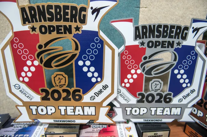 Zwei Auszeichnungen für das Taekwondo-Turnier „Arnsberg Open 2026“ liegen übereinander. Die Auszeichnungen zeigen ein Taekwondo-Symbol und den Schriftzug „TOP TEAM“. Darunter liegen weitere Medaillen und Urkunden.