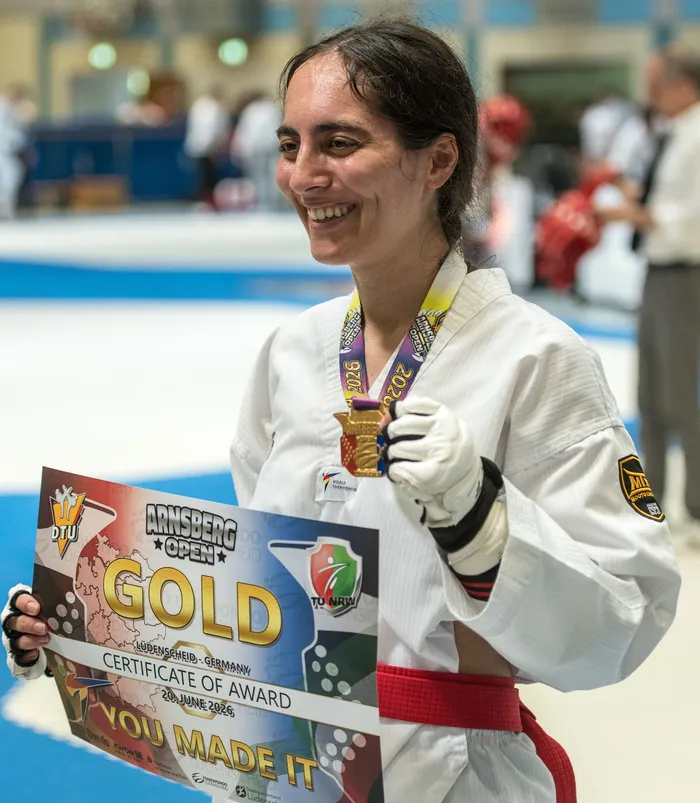 Eine lächelnde Taekwondo-Athletin hält eine Goldmedaille und eine Urkunde mit der Aufschrift 