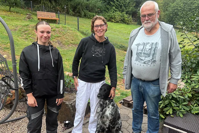 Laura Igel, Britta Wortmann und Ralph Born stehen im Garten neben einem schwarz-weiß gefleckten Hund.