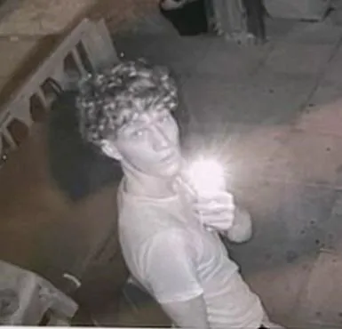 Ein junger Mann mit lockigem Haar hält eine helle Taschenlampe in die Kamera.