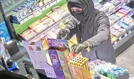 Maskierter Täter füllt in einem Kiosk eine Tasche mit Zigarettenpackungen.