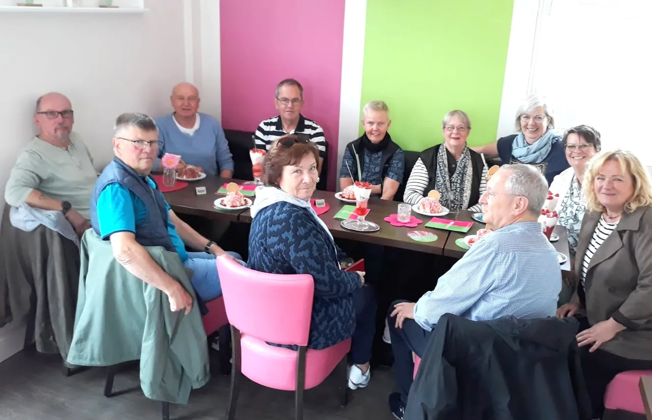 Eine Gruppe von etwa zehn Personen sitzt um einen Tisch und isst Eis. Sie scheinen sich in einem Besprechungsraum zu befinden, die Wände sind in Rosa und Grün gestrichen.