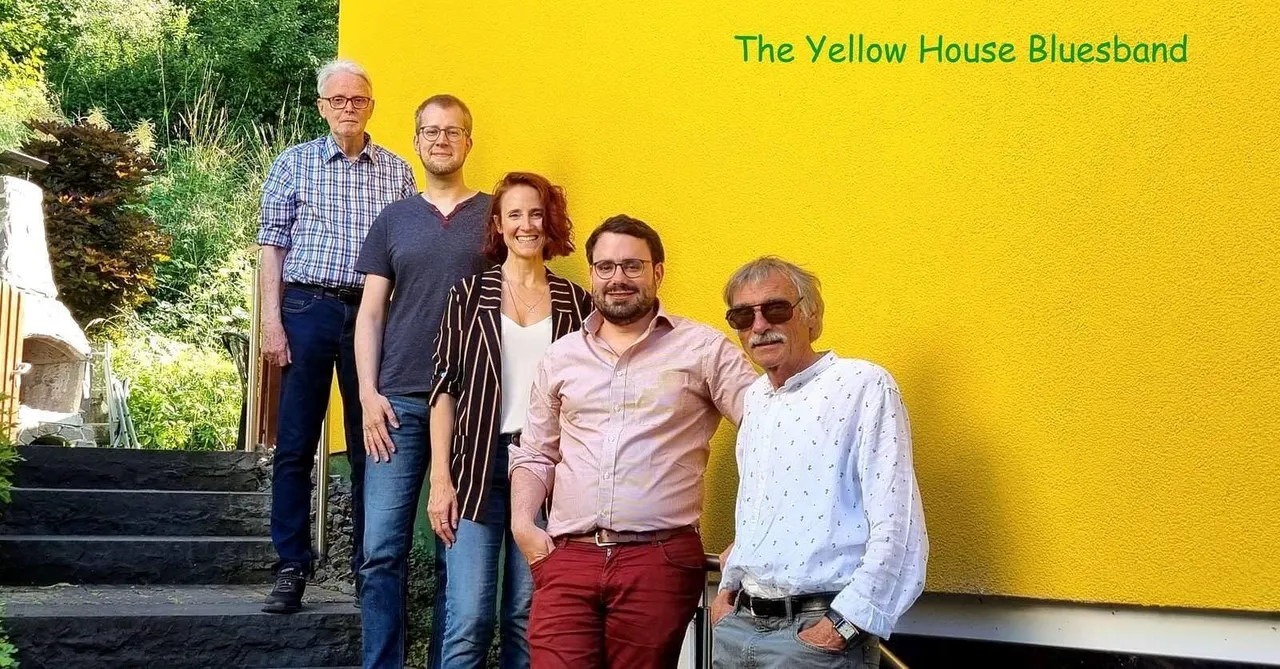 Die fünf Mitglieder der Yellow House Bluesband stehen vor einer leuchtend gelben Wand mit dem Bandnamen.