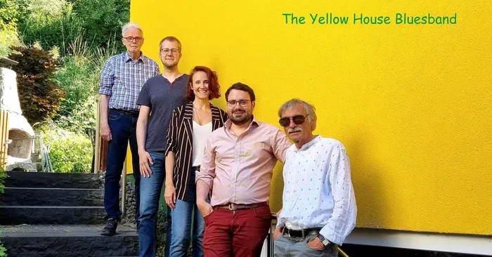 Die fünf Mitglieder der Yellow House Bluesband stehen vor einer leuchtend gelben Wand mit dem Bandnamen.
