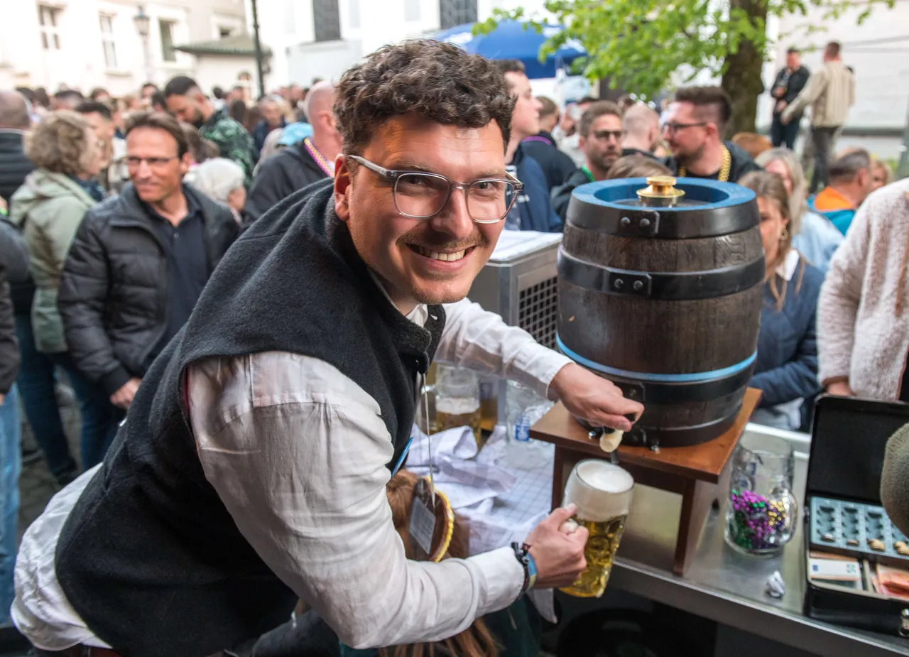 Ein lächelnder Mann mit Brille zapft auf der Thekentour in Lüdenscheid Bier aus einem kleinen Holzfass. Im Hintergrund sind viele Menschen zu sehen.