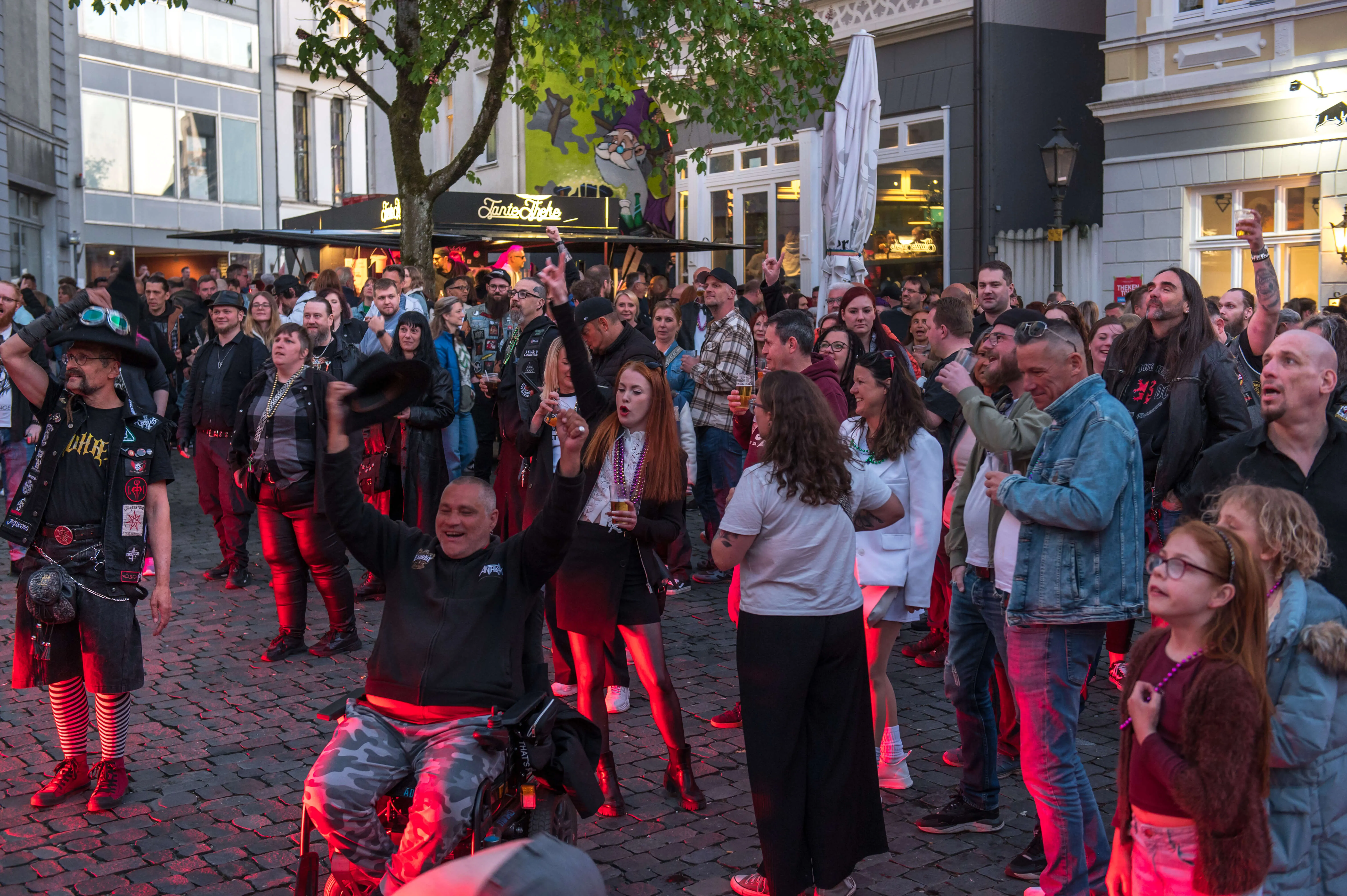 Große Menschenmenge auf einem belebten Platz vor Kneipen und Restaurants, viele tragen Lederjacken und genießen Getränke.