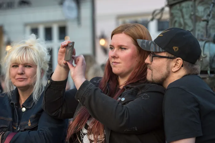 Drei junge Erwachsene fotografieren mit einem Smartphone während der Thekentour in Lüdenscheid. Im Hintergrund sind weitere Menschen und Gebäude zu sehen.
