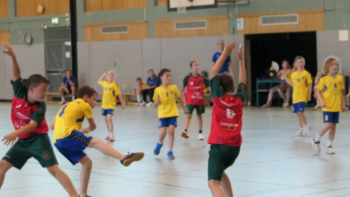 Handballspiel der E-Jugend: Spieler in roten und grünen Trikots kämpfen um den Ball gegen ein Team in gelben Trikots in einer Sporthalle.