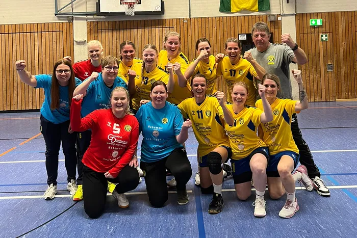 Eine Gruppe jubelnder Handballerinnen des TuS Plettenberg in gelben, blauen und roten Trikots posiert in einer Sporthalle.